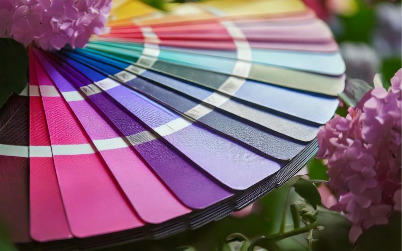 Fächer mit Wandfarben in kräftigen und dezenten Farbtönen von Pink über Blau bis Grün, umgeben von Blumen – Inspiration für die individuelle Raumgestaltung.