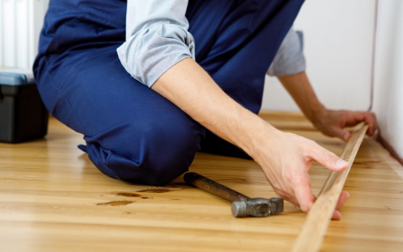 Montage- und Tapezierzubehör für präzise Arbeiten: links die sorgfältige Anbringung einer Sockelleiste mit Hammer und Werkzeug als Teil des Montagezubehörs, rechts typische Helfer wie Tapezier- und Malerzubehör für exaktes und sauberes Arbeiten an Wand und Boden 