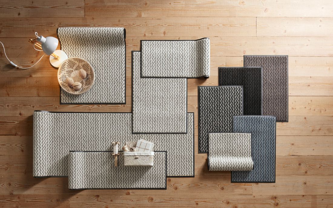 Vielfältige Wash und Dry Fußmatten: links eine bunte Matte im Tigerkopf-Design am Treppenaufgang, rechts eine Auswahl an dekorativen Fußmatten mit Schaf-, Blumen- und grafischen Mustern in Grün-, Grau- und Blautönen, kombiniert mit Wohnaccessoires.